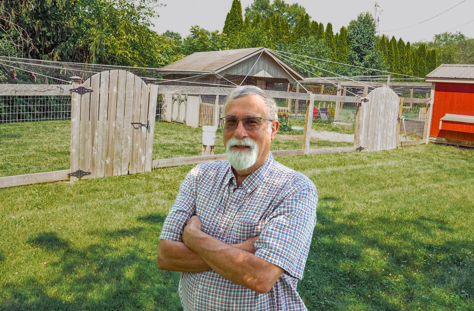 Gary Watson stands in his yard in front of his chicken run, protected from predators by bird netting and wooden fencing.